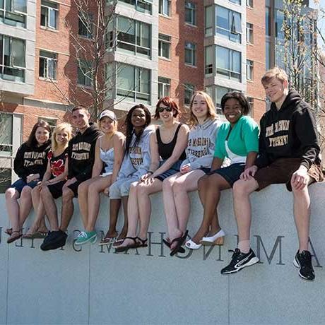 Group of students sitting on a wall that reads, "Framingham State University"